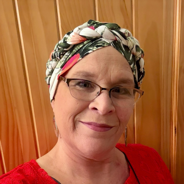 Woman wearing a colorful headscarf and glasses against a wooden panel background